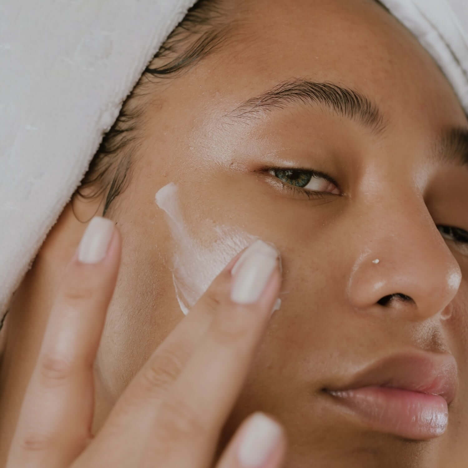 Applicazione di crema idratante per cosmetici per pelle secca su viso di donna con asciugamano