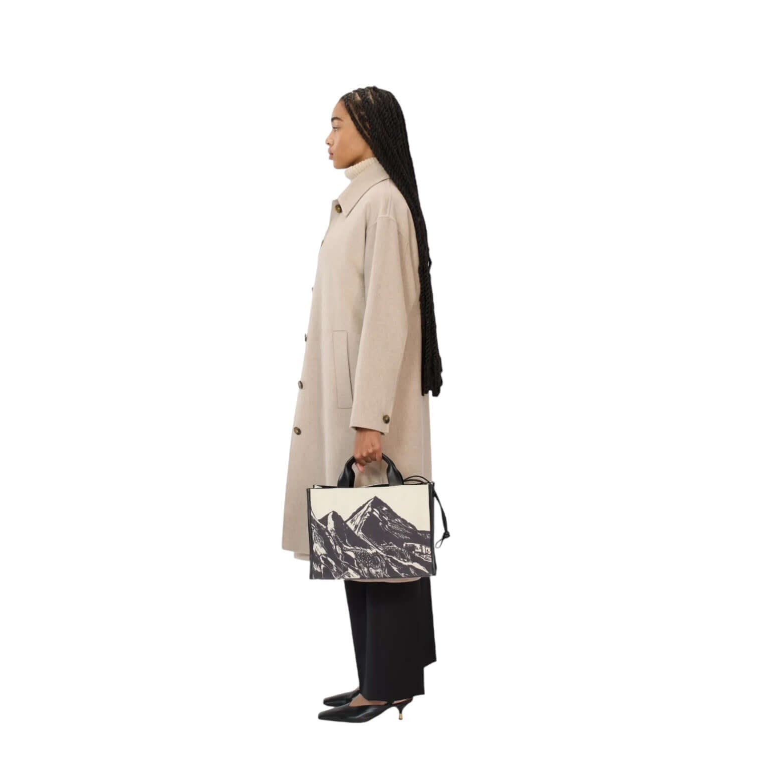 Model in a stylish beige coat holding the Nomade Montagne bag, showcasing versatile fashion.