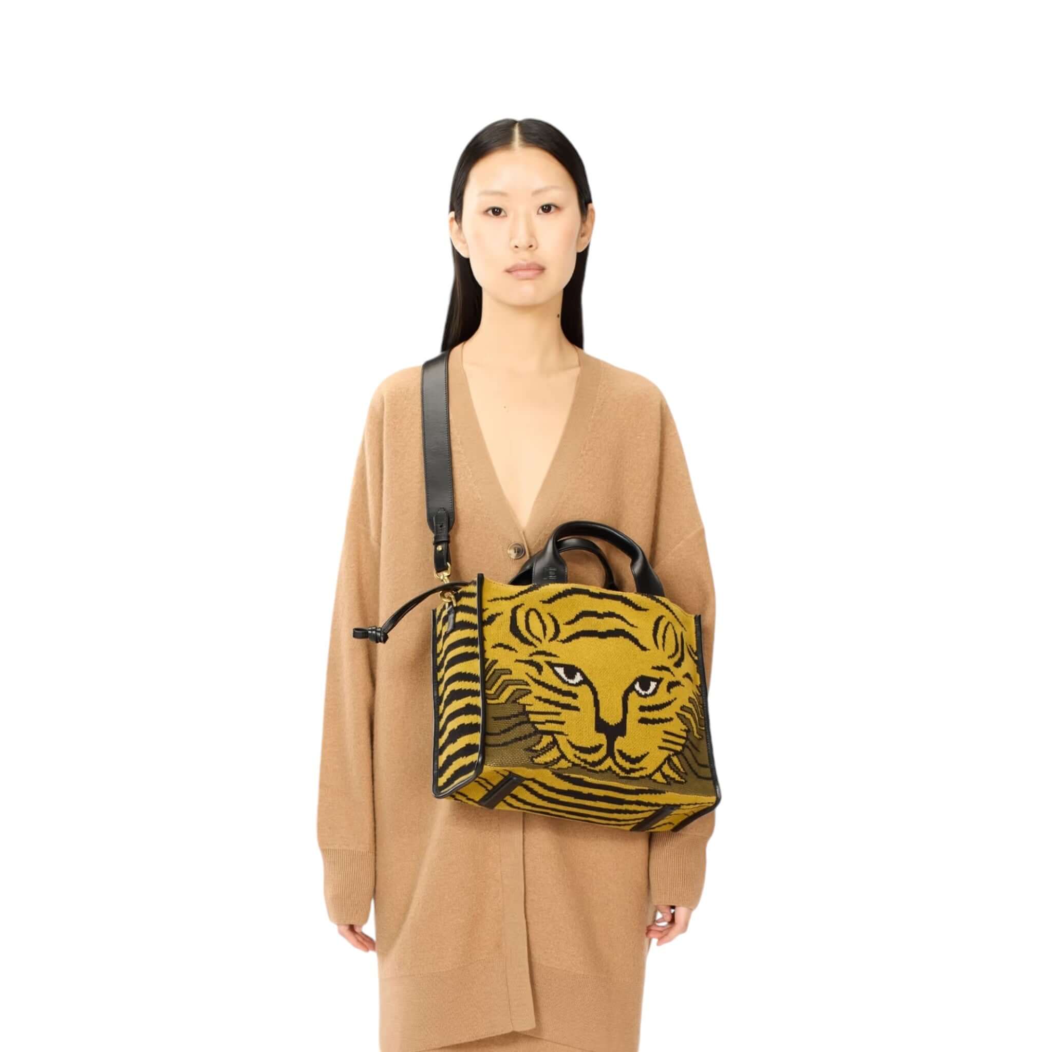 Model showcasing a tiger print handbag, featuring a shoulder strap and top handles, styled in a cozy brown outfit.