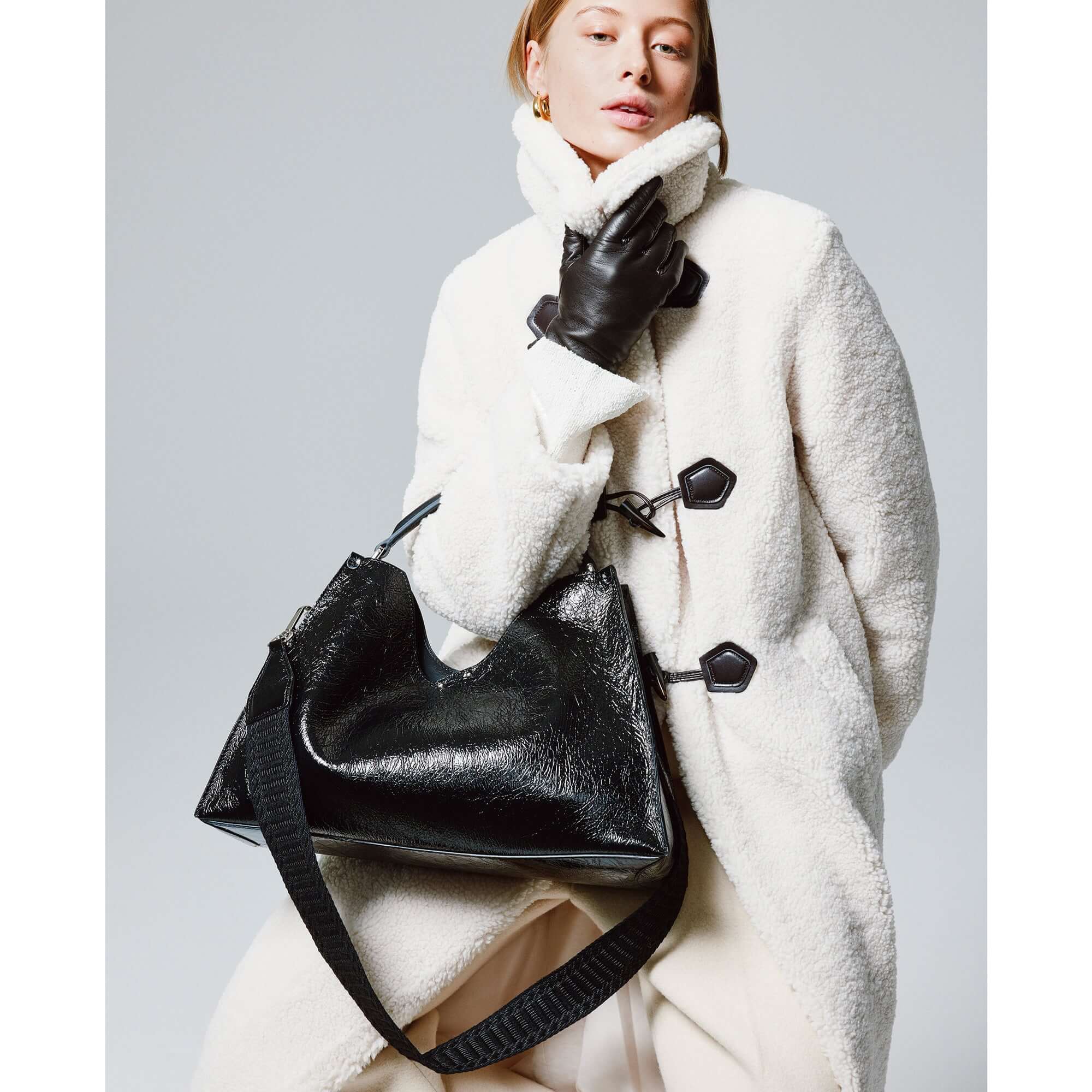 Model wearing a stylish white coat with black gloves, holding a black leather handbag, showcasing contemporary fashion.