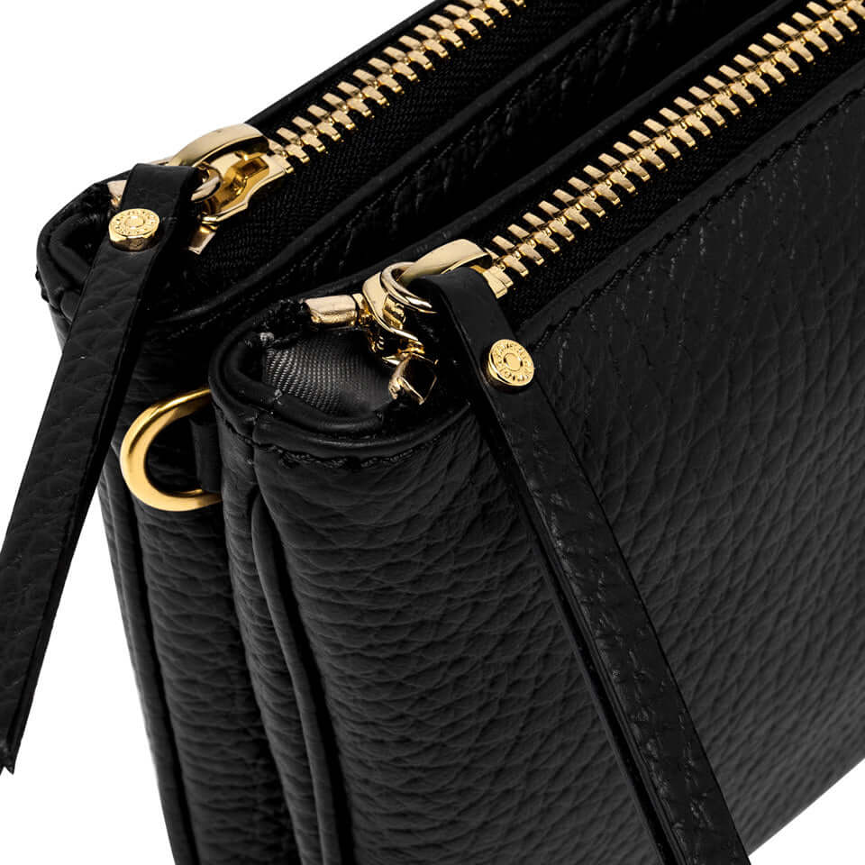 Detail of Frida black leather crossbody bag with gold zippers and textured finish, showcasing double compartments.