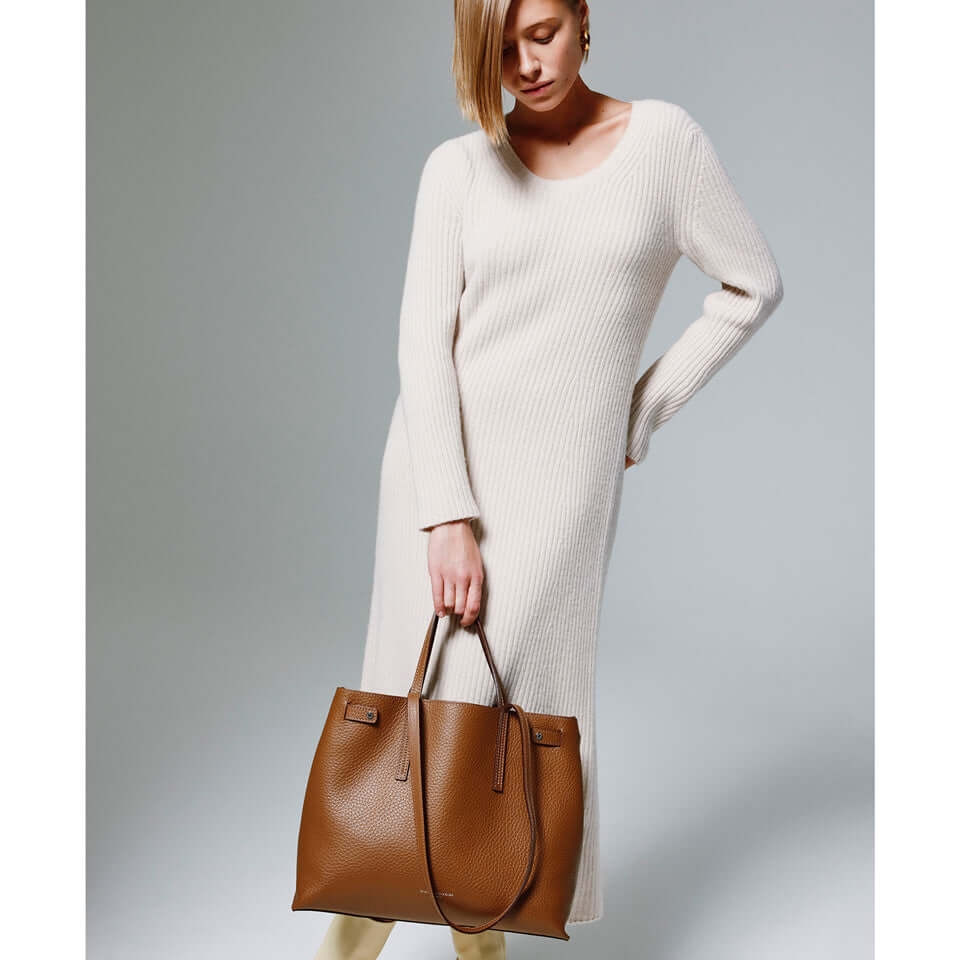 Model showcasing Altea handbag in brown leather, paired with a cream sweater dress, emphasizing timeless design.