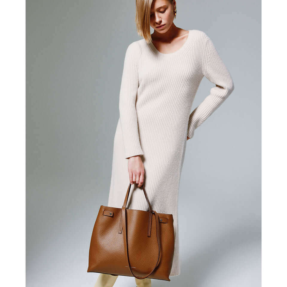 Model wearing a cozy cream dress, holding the brown Altea leather bag, featuring a timeless design and practicality.