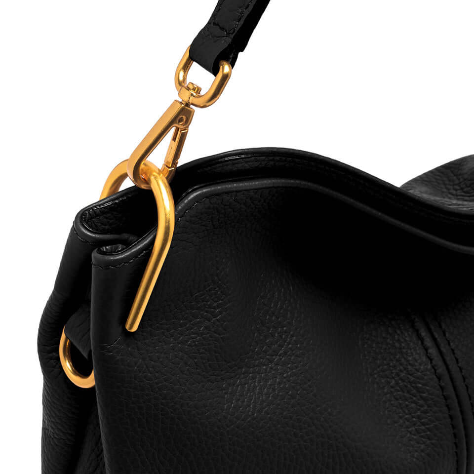 Close-up of gold metal clasp on black leather shoulder bag, showcasing its sleek design and quality craftsmanship.