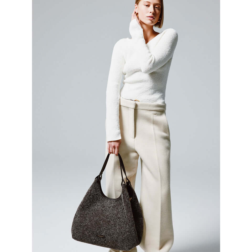 Model showcases the DUA handbag in suede, paired with a white top and cream trousers, highlighting its stylish versatility.