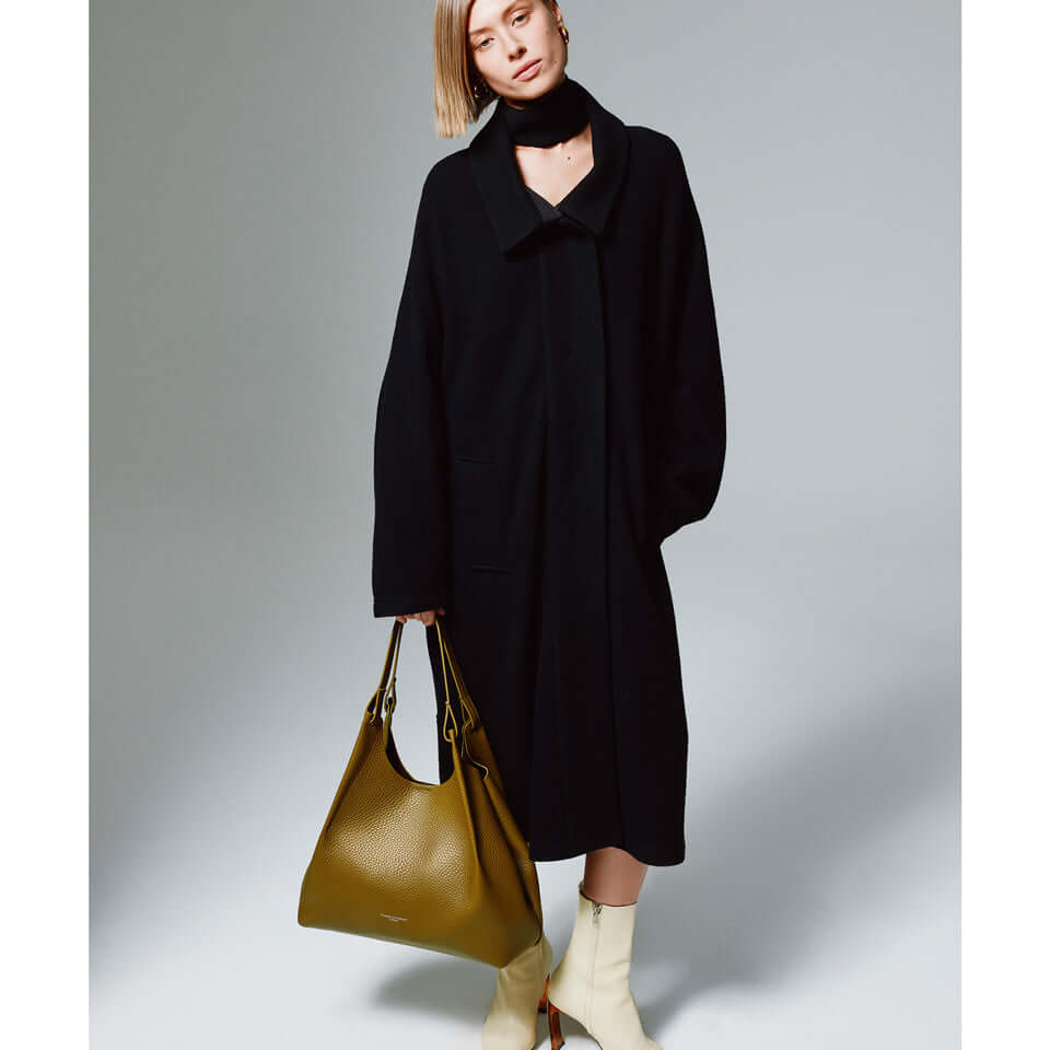Model wearing a stylish black coat, holding a DUA leather bag, showcasing elegant fashion and accessories.