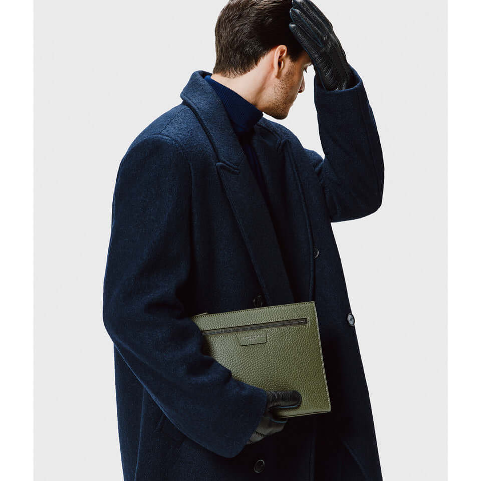 Man in a navy coat holding a stylish green leather pochette, showcasing modern and timeless design.