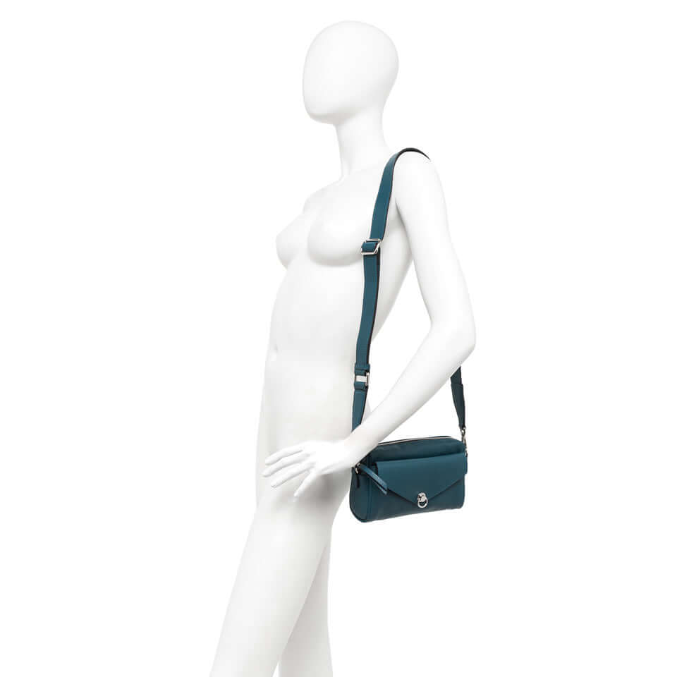 Deva bag in teal leather, showcasing its rectangular shape and removable cross-body strap on a mannequin.