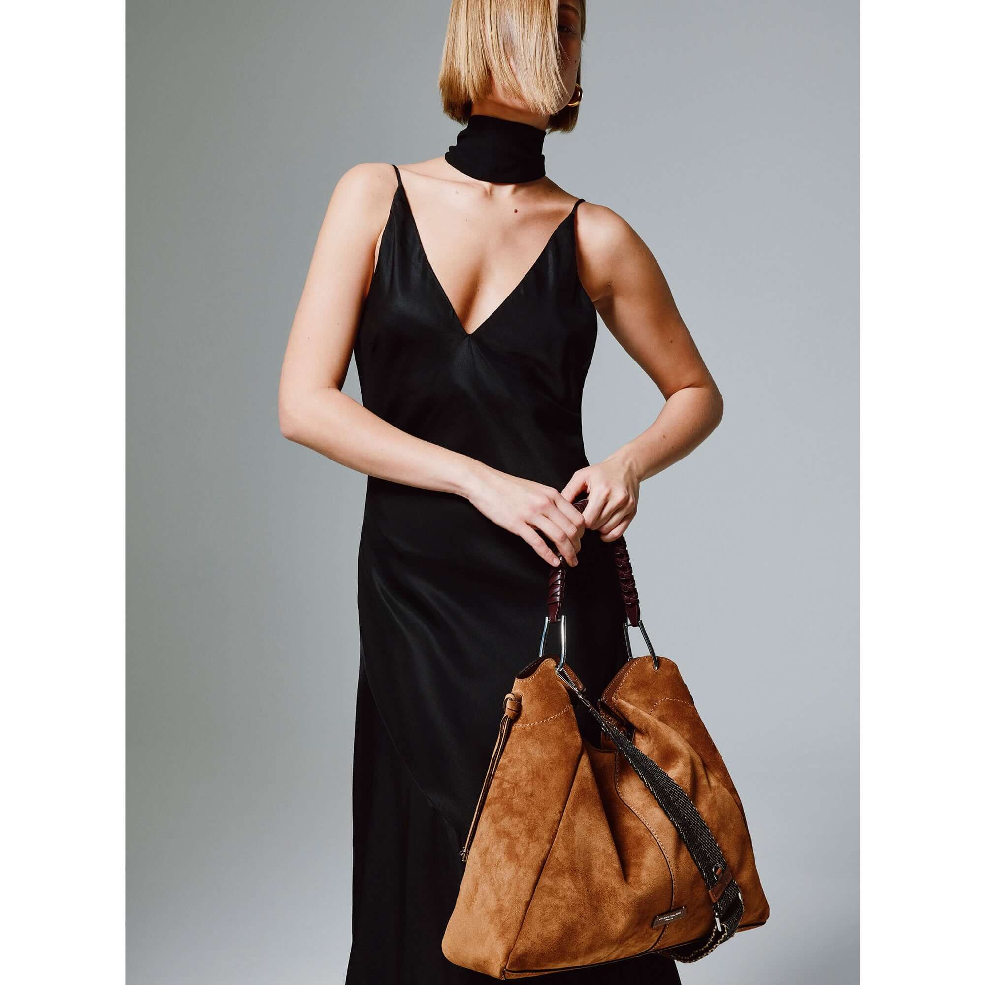 Model wearing a black dress while holding the Era bag by Gianni Chiarini in suede, showcasing its stylish design.