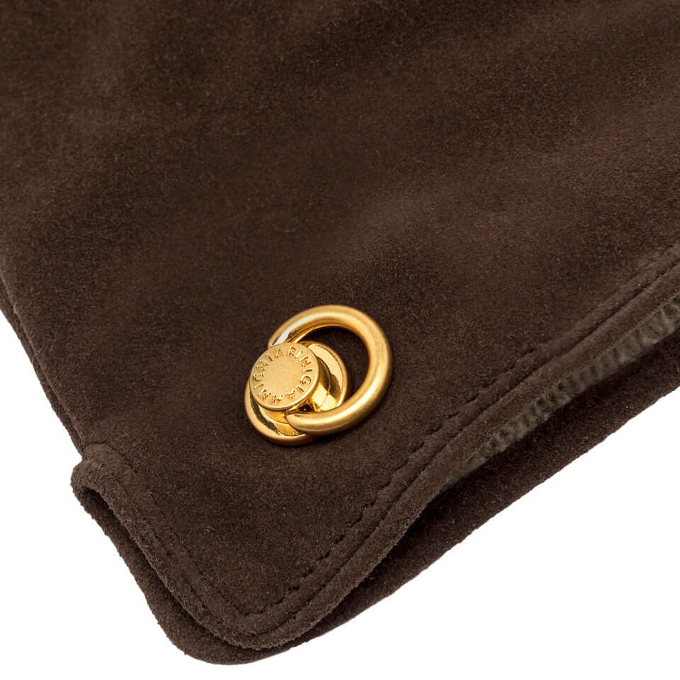 Dettaglio dei guanti in camoscio marrone con chiusura elegante in metallo dorato.