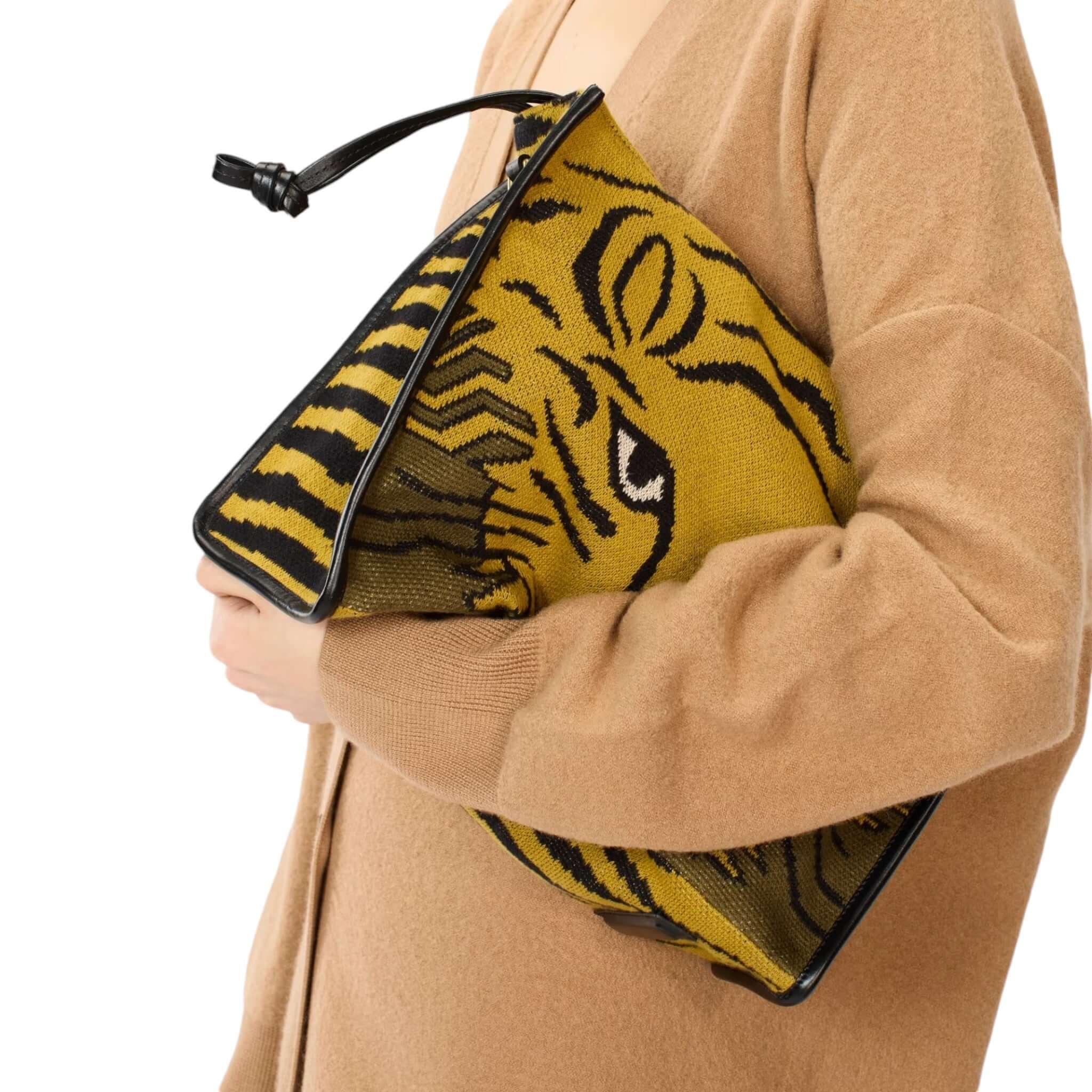 Stylish person holding a yellow tiger print clutch bag with black trim, showcasing a unique design.
