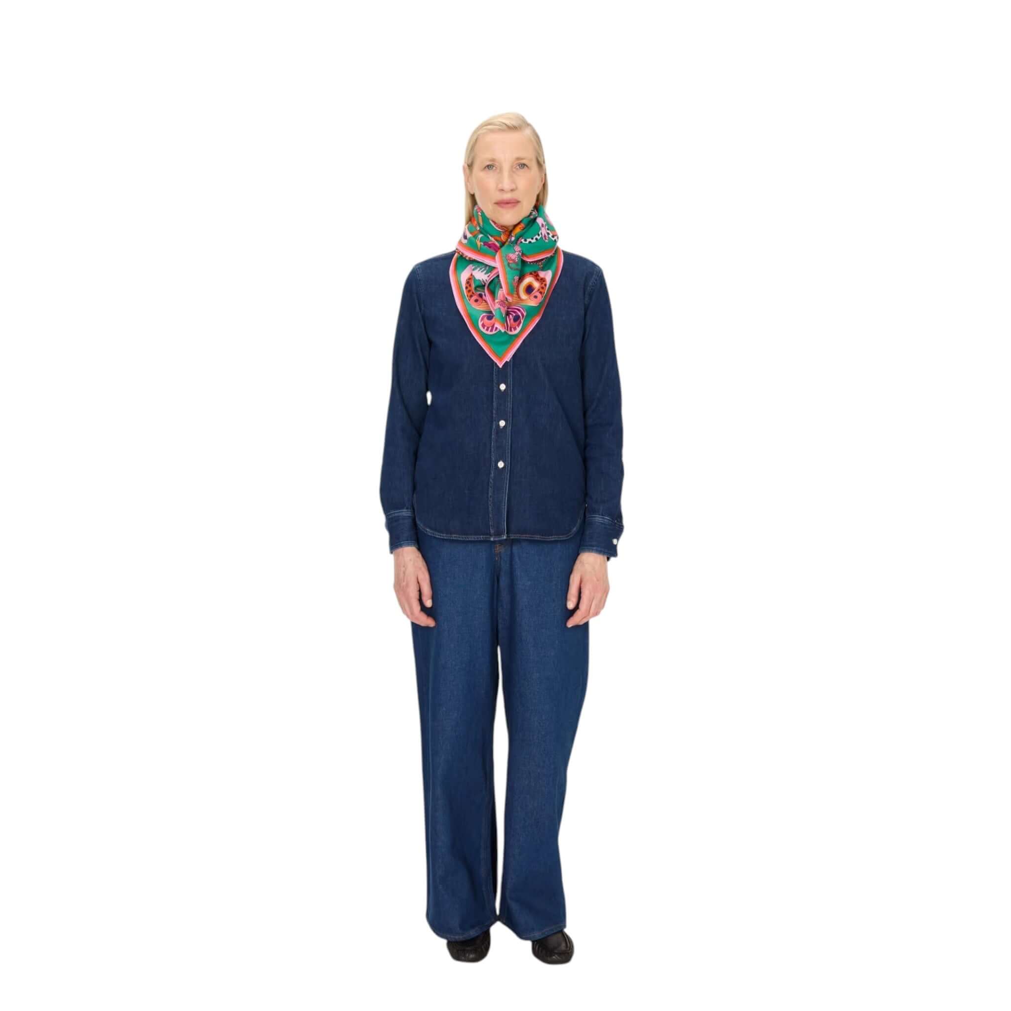 A woman wearing a denim outfit and a colorful handmade square botanical scarf around her neck.
