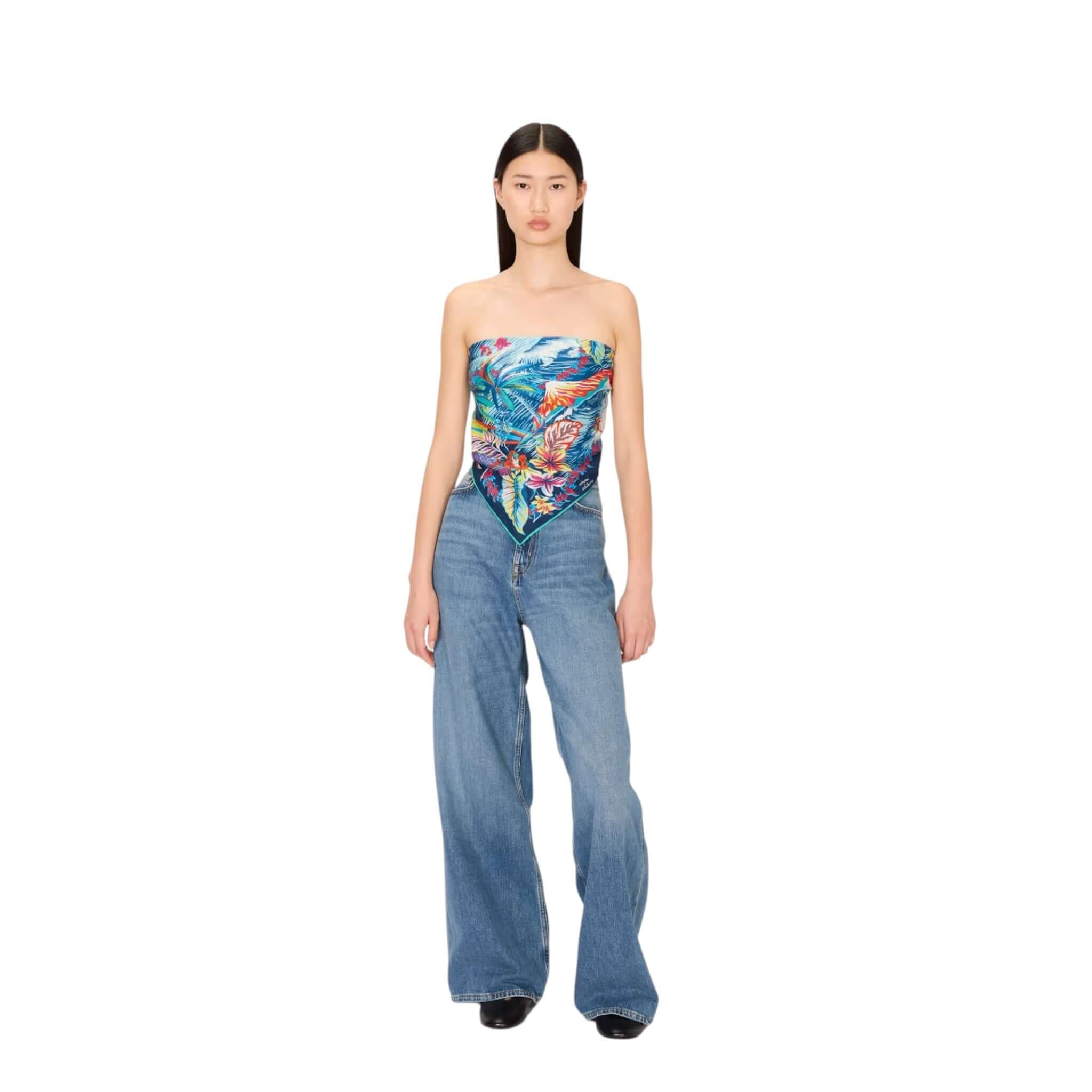Model wearing a colorful Hawaii-inspired square scarf as a top with flared jeans, showcasing vibrant tropical prints.