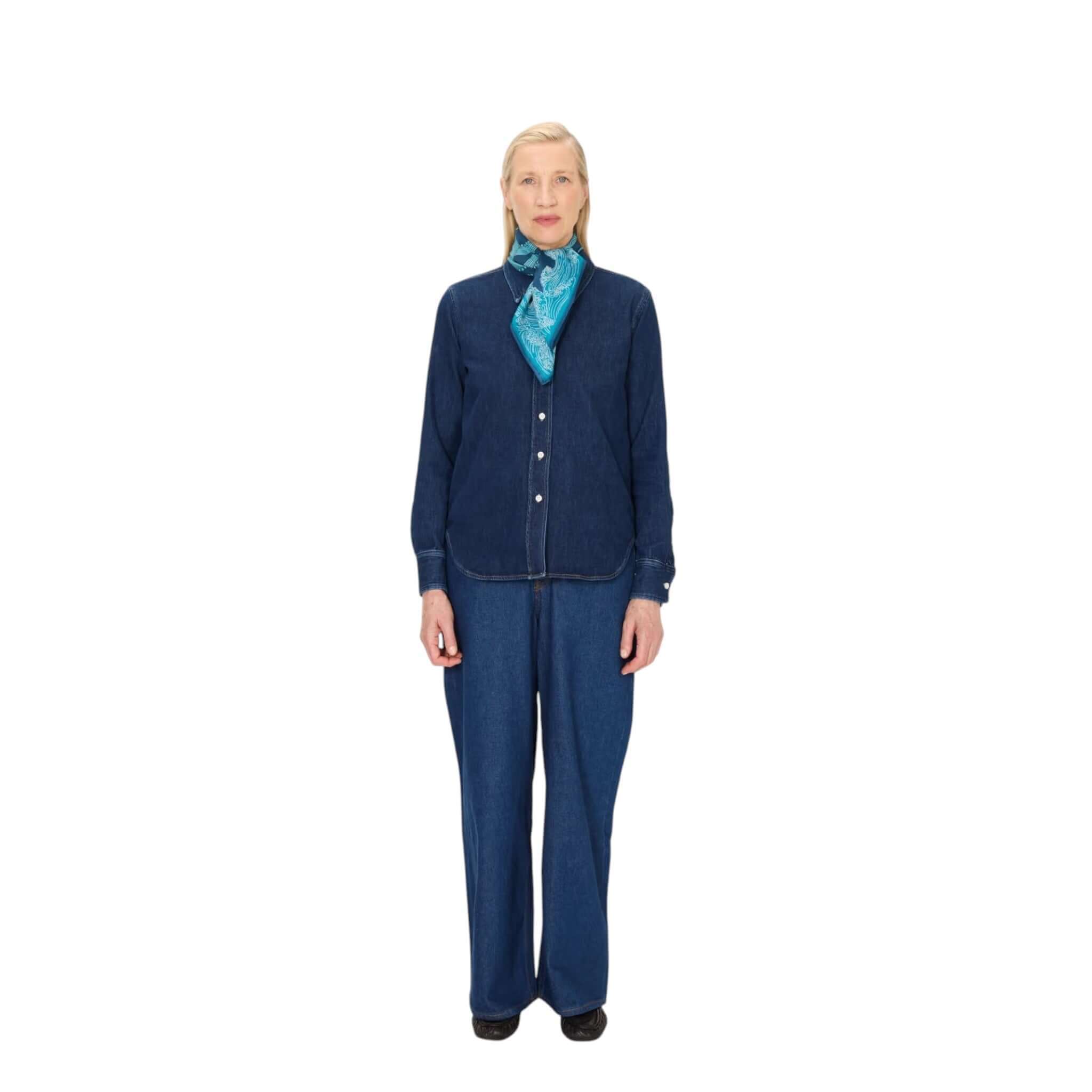 Woman wearing a denim outfit with a blue Foulard Quadrato Poseidon scarf, showcasing versatile styling and elegance.