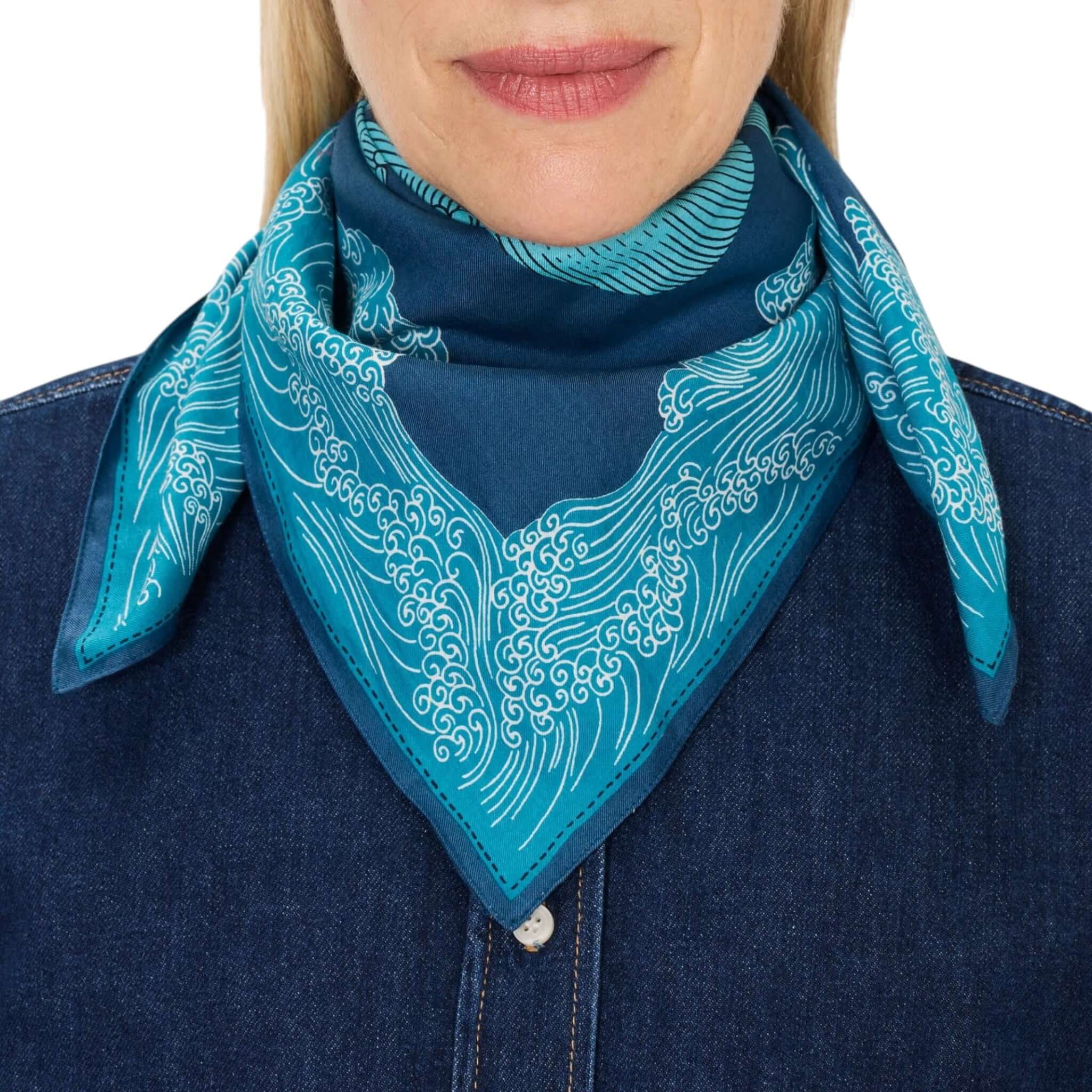 Foulard Quadrato Poseidon indossato al collo, con elegante stampa ondulata in blu turchese.
