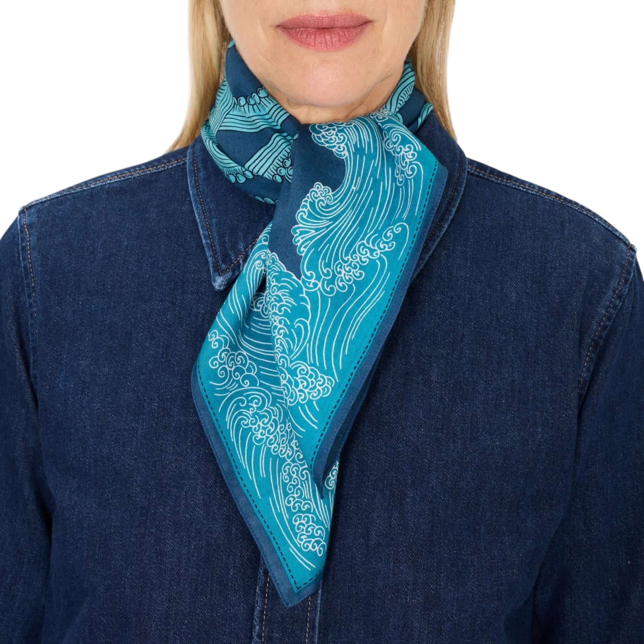 Foulard Quadrato Poseidon indossato come sciarpa, con design ondulato in tonalità blu e verde. Elegante e versatile.