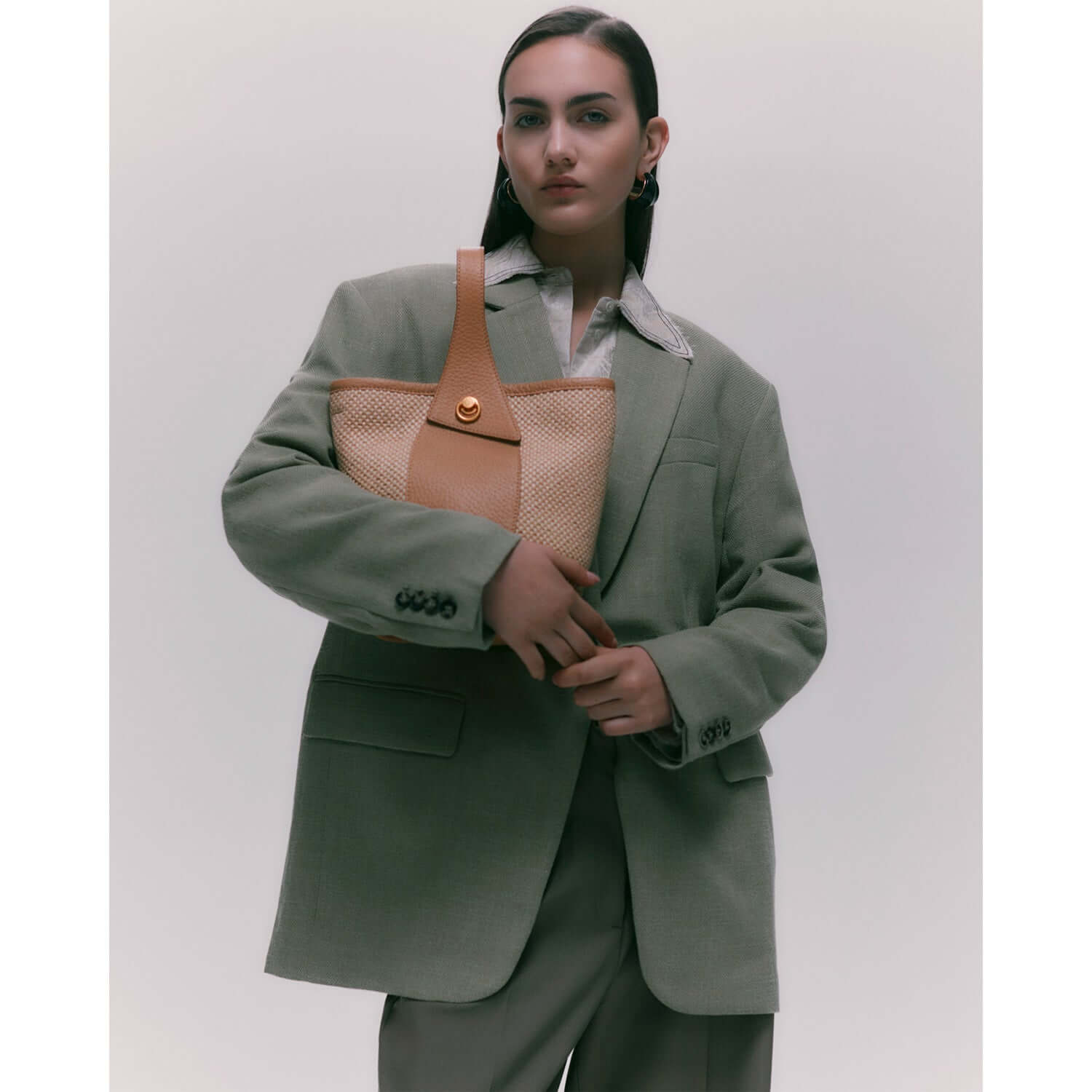 Model wearing a chic green blazer holding Gianni Chiarini Firenze Ester straw bucket bag, showcasing its versatile design.