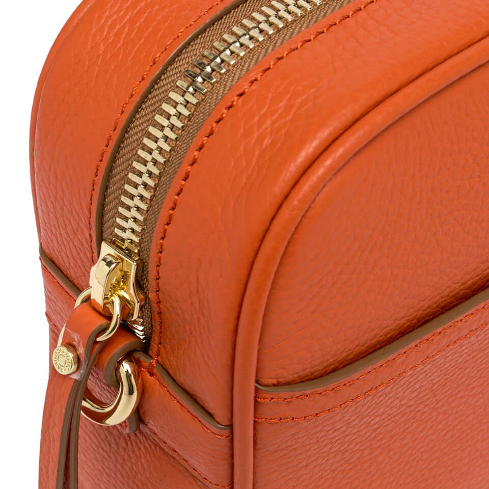 Close-up of Nina bag's orange textured leather and gold zipper detailing, showcasing quality craftsmanship.