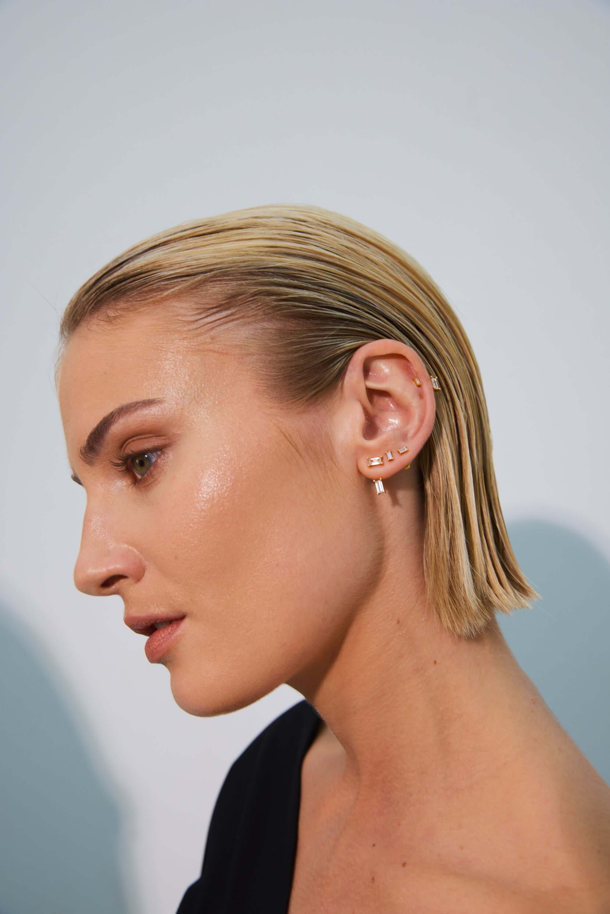 Profile view of a woman with sleek blonde hair, showcasing multiple elegant earrings.