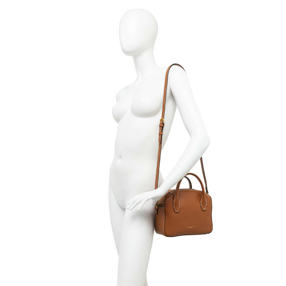 Small brown leather bowling bag Sabrina, with double handles and shoulder strap, displayed on a mannequin.