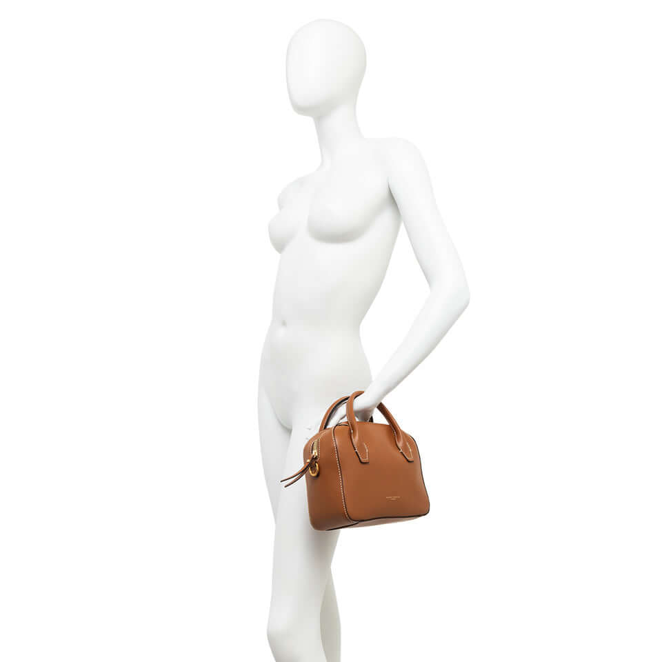 Small brown bowling bag, Sabrina, displayed on mannequin, showcasing its timeless design and compact size.