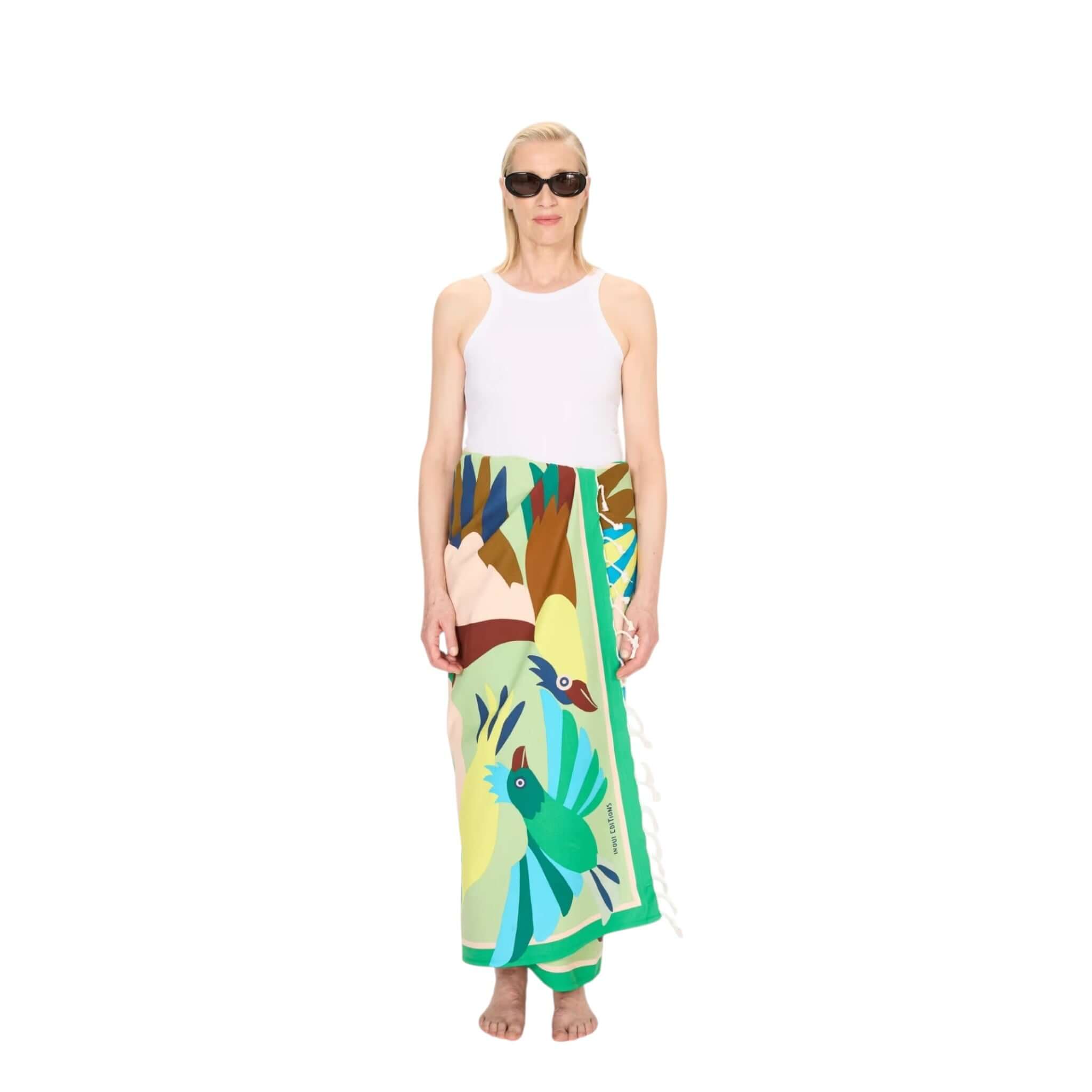 Woman wearing Telo Mare Voyage beach towel with colorful bird designs. 100% cotton, 100 x 190 cm, handmade in India.