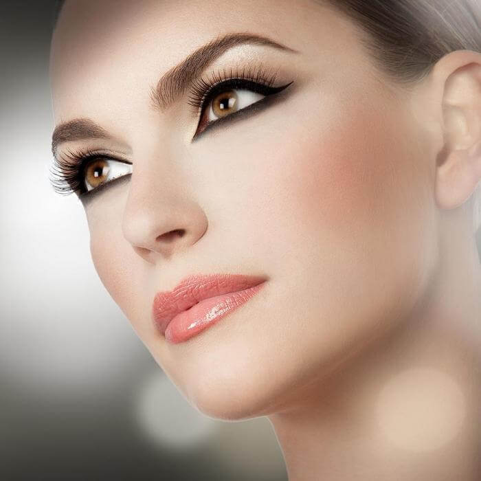 Close-up of a woman showcasing sharp eyeliner, voluminous lashes, and glossy lips for a stunning beauty look.