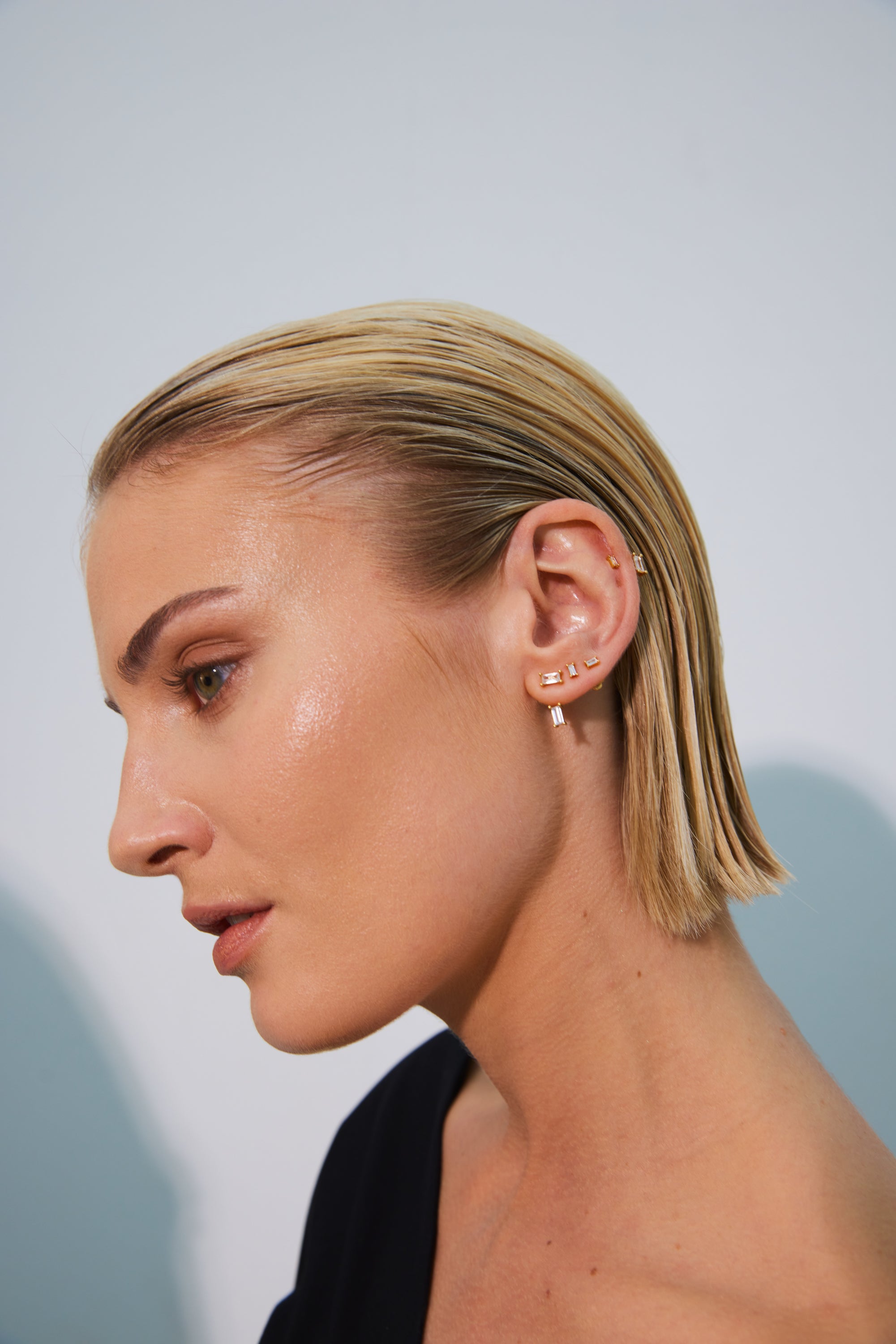 Profile view of a woman with sleek blonde hair, showcasing multiple elegant earrings.