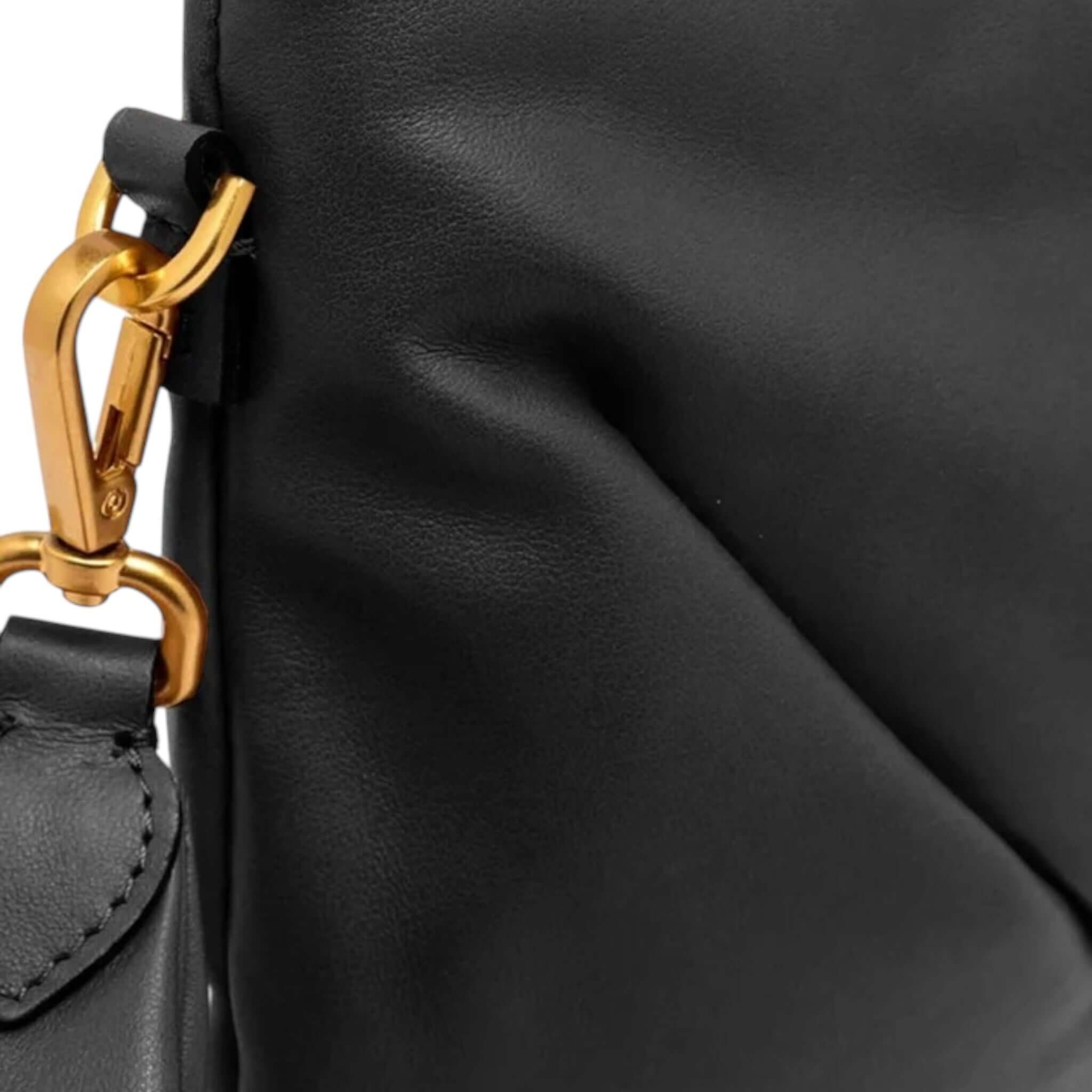 Close-up of Allegra clutch showing smooth black leather and decorative gold chain strap attachment.