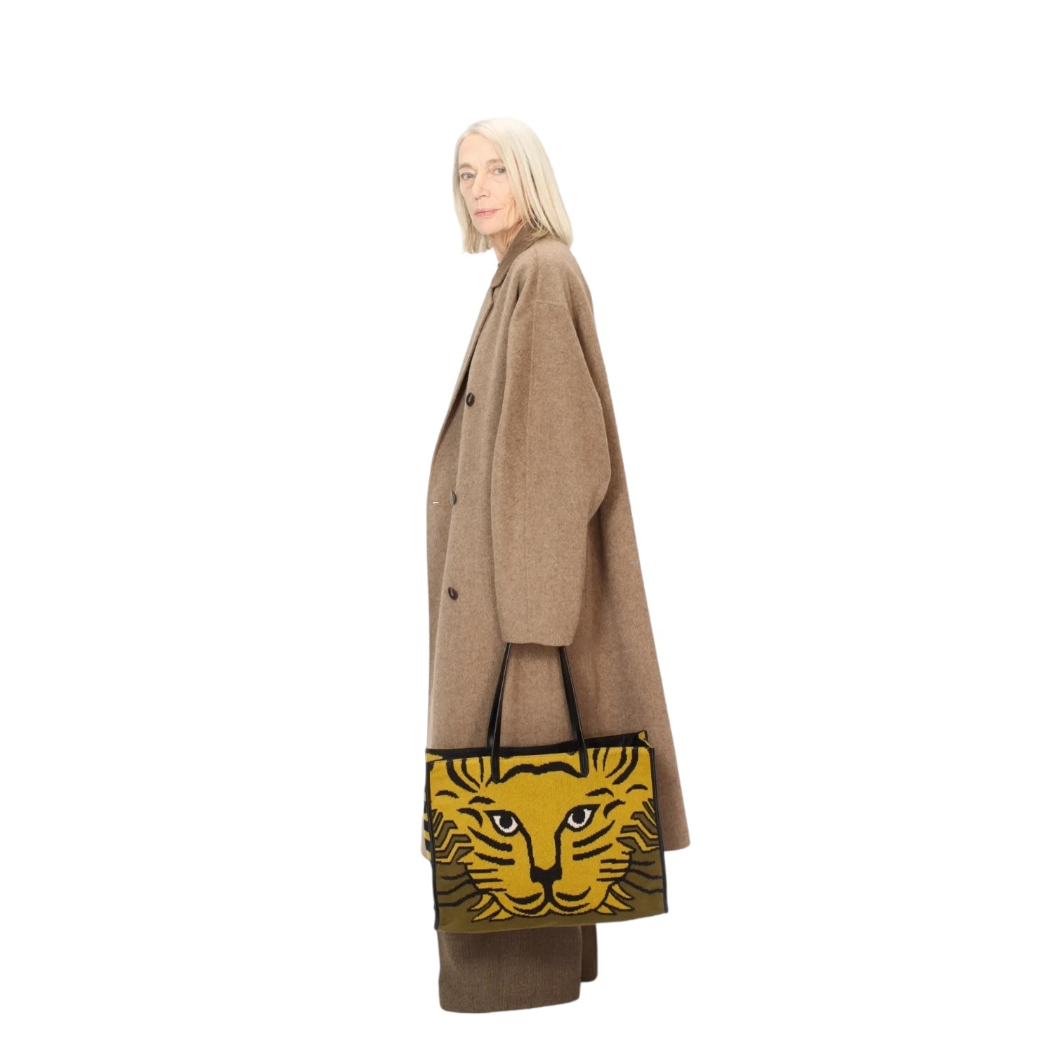 Woman in a stylish brown coat holding a leopard print tote bag from the side.