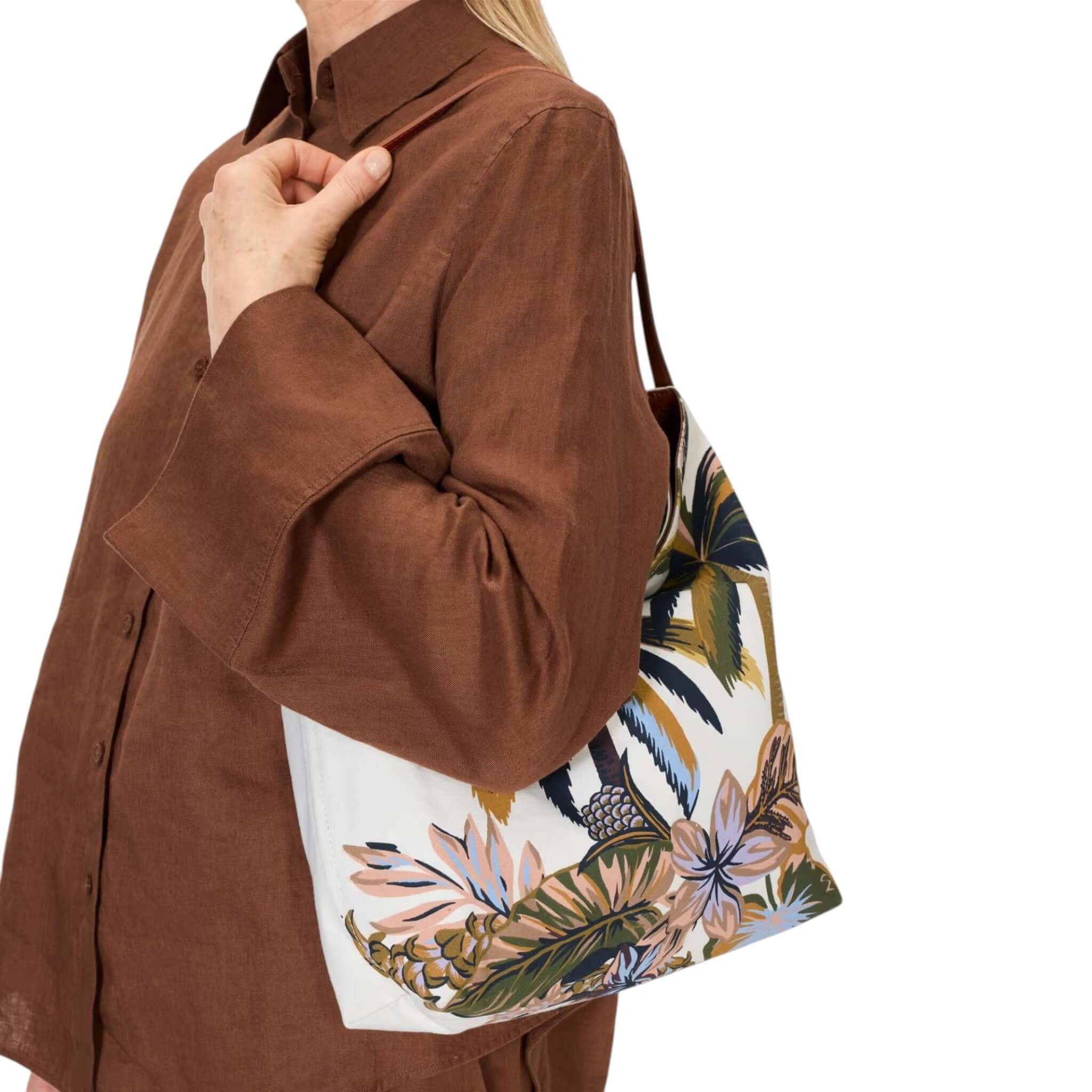 Borsa Campus Hawai: borsa in cotone, design minimalista e fiori tropicali, indossata con una camicia marrone.