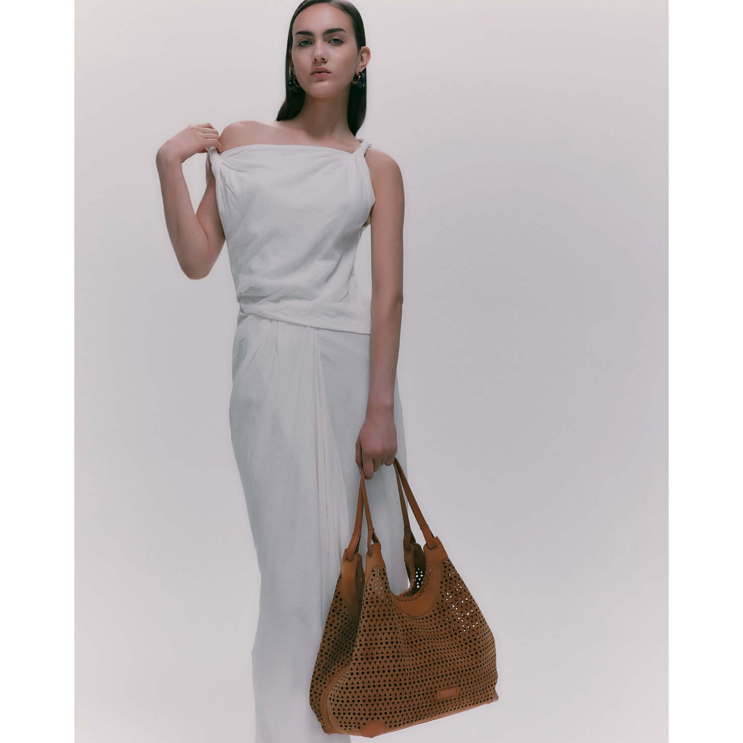 Model showcasing the DUA bag, a contemporary design in suede with perforated detailing, paired with an elegant white outfit.