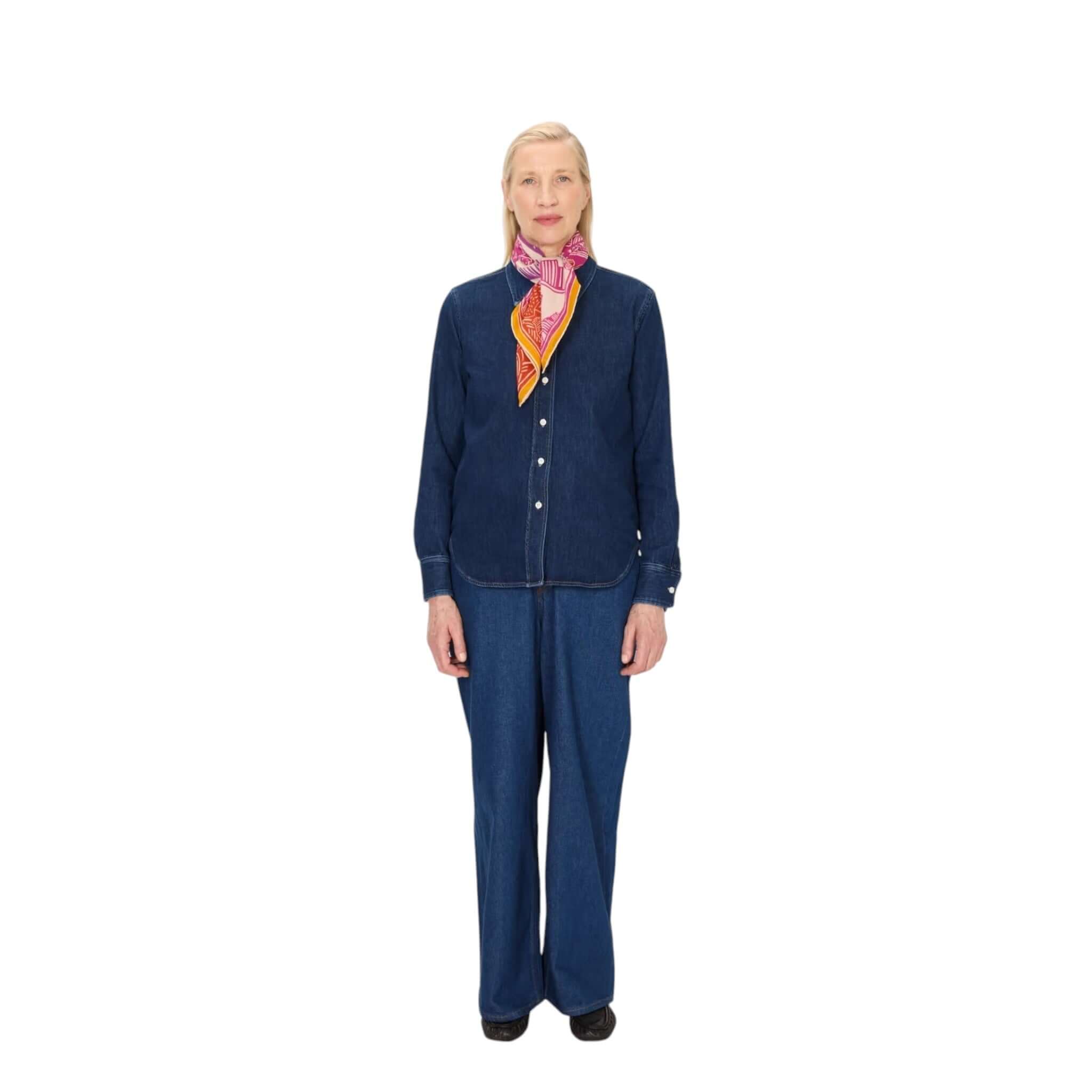 A woman wearing a denim outfit with a vibrant, hand-printed Jungle square scarf around her neck.