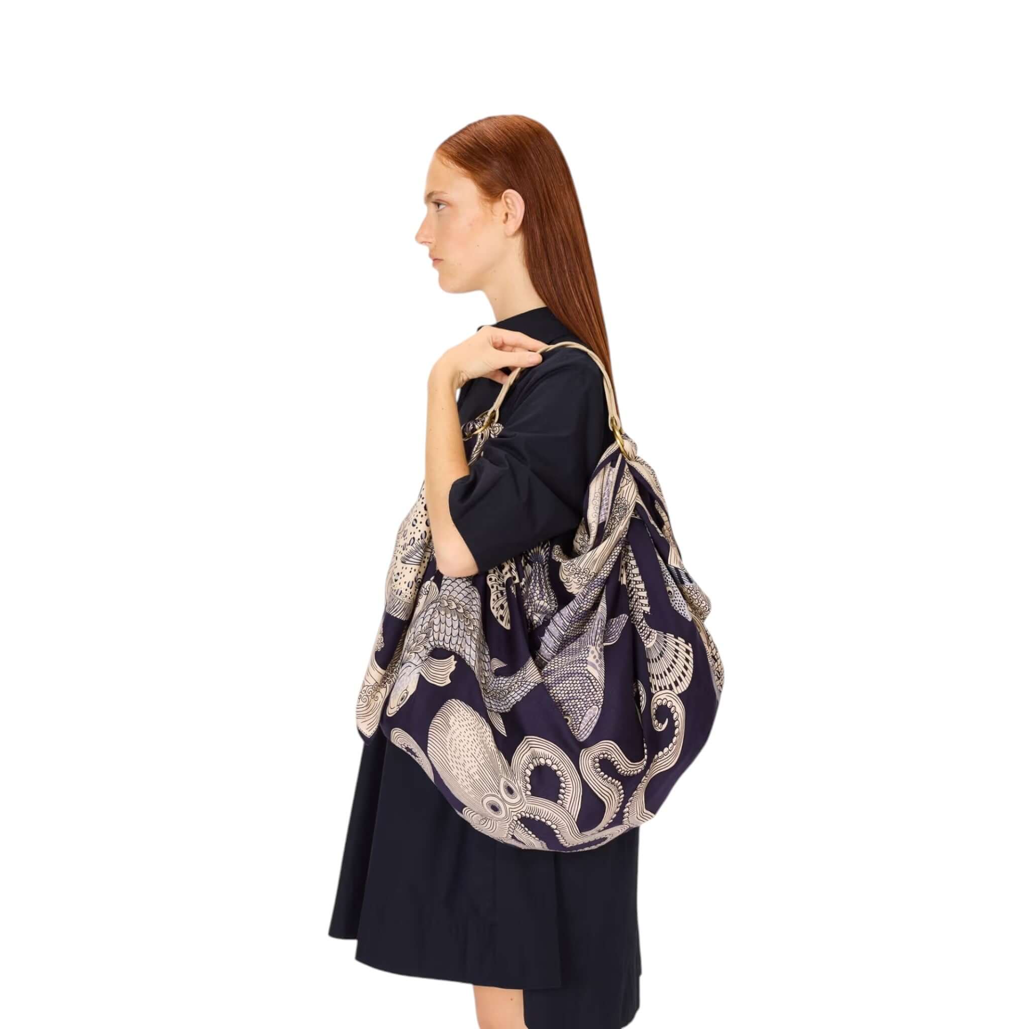 Elegante borsa con motivo di polpi in tonalità scure, indossata da una donna con capelli rossi.