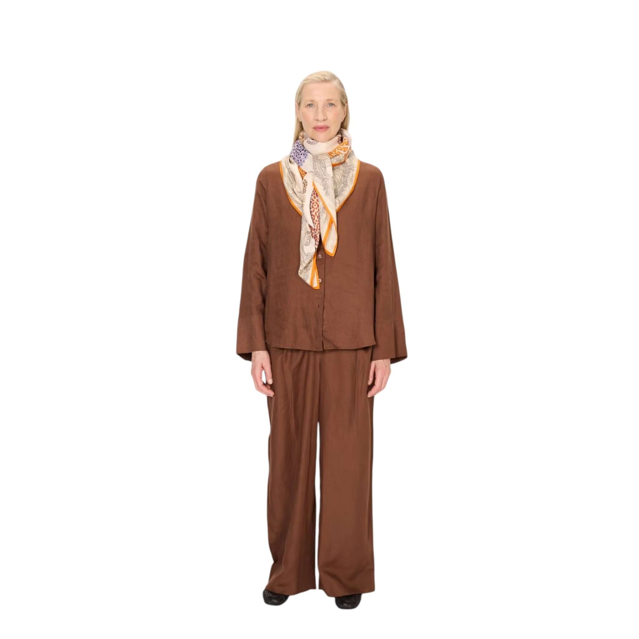 Model wearing brown outfit with Foulard Quadrato Poseidon silk scarf, showcasing elegant draping and vibrant colors.