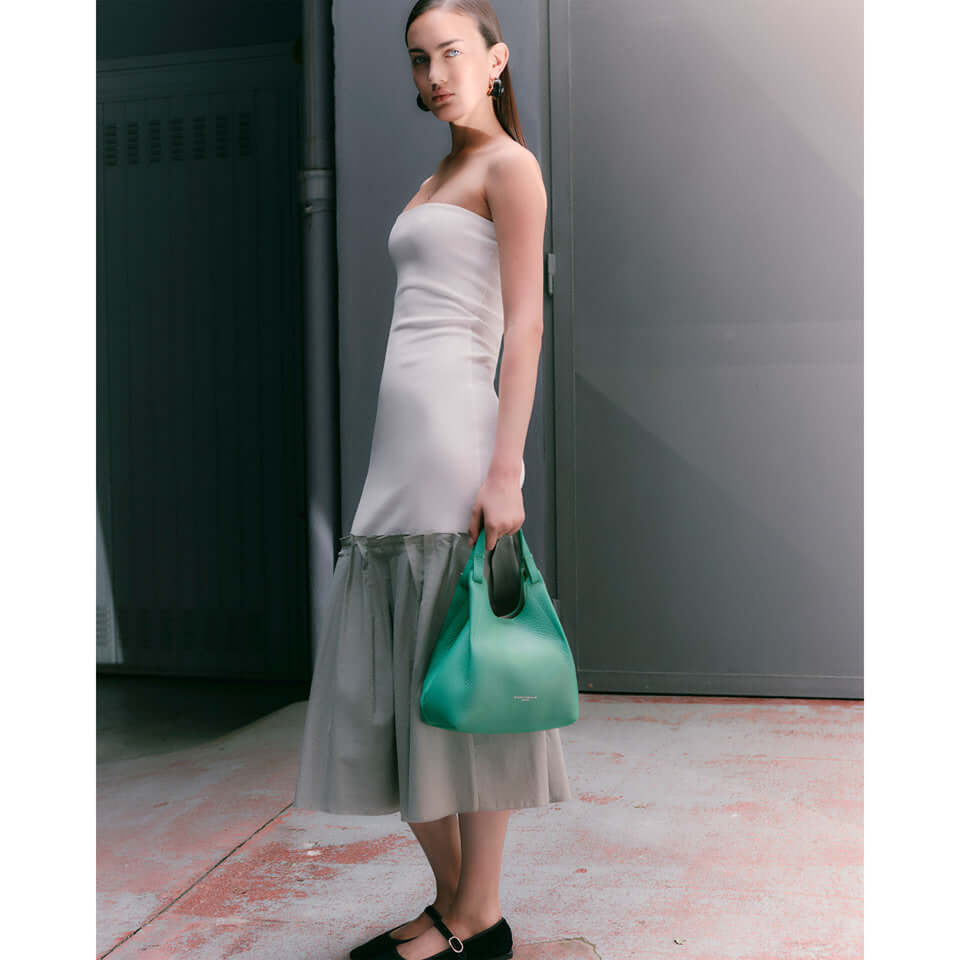 Model wearing a sleek dress and showcasing the DUA handbag in vibrant green, perfect for any stylish look.