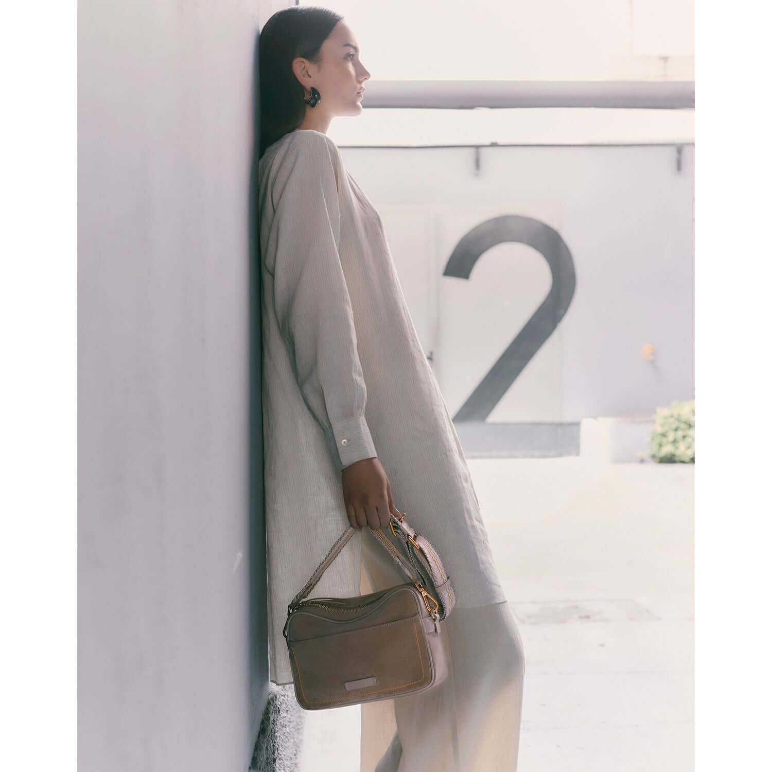 Woman in a beige outfit holding the NINA crossbody bag by Gianni Chiarini against a modern backdrop.