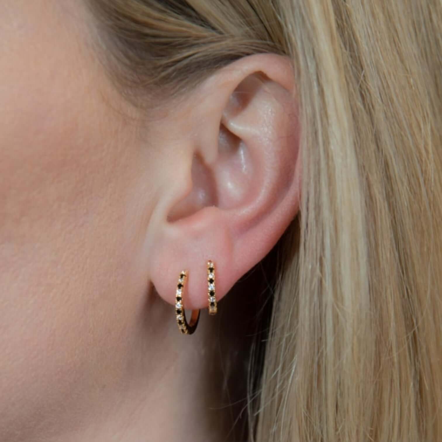 Small white and black hoop earrings in gold-plated brass worn by a woman, showcasing elegance and style.