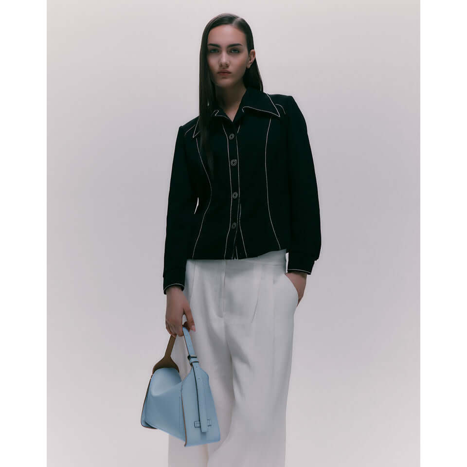 Model wearing a black jacket and white pants, holding a light blue handbag.