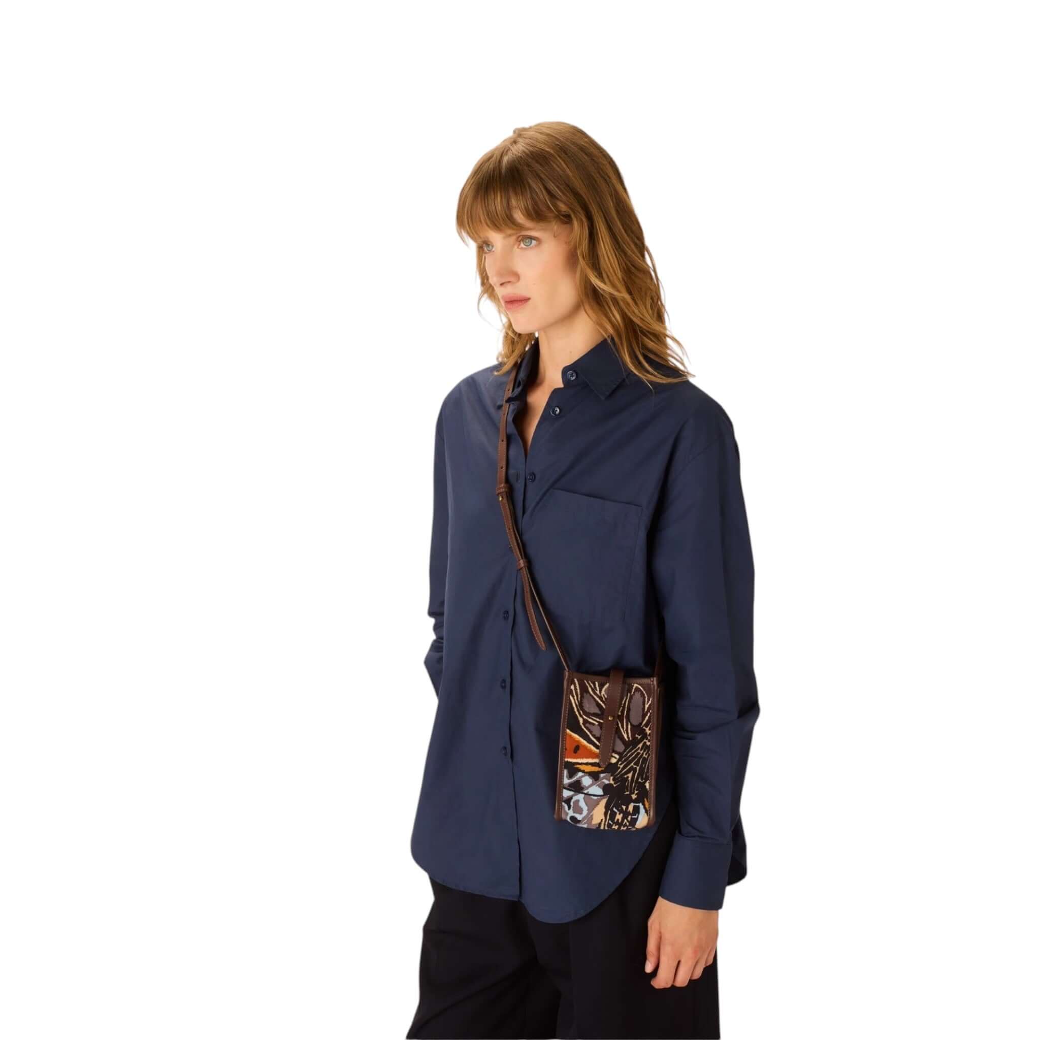 Modella che indossa la custodia Caprice Farfalle con una camicia blu. Design iconico in pelle italiana.