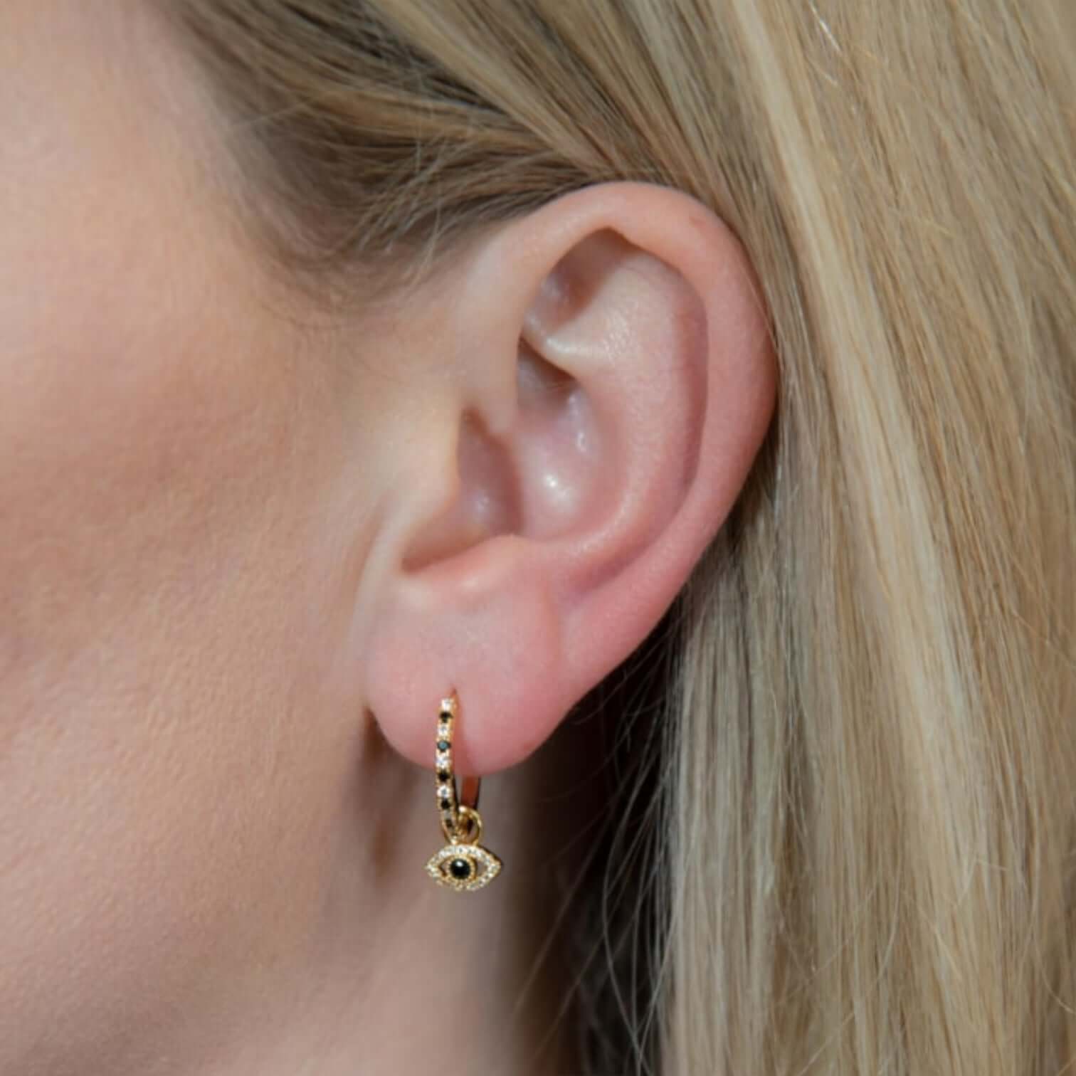 Sabrina Charm: gold plated brass hoop earrings with eye design, elegantly worn on a woman's ear.