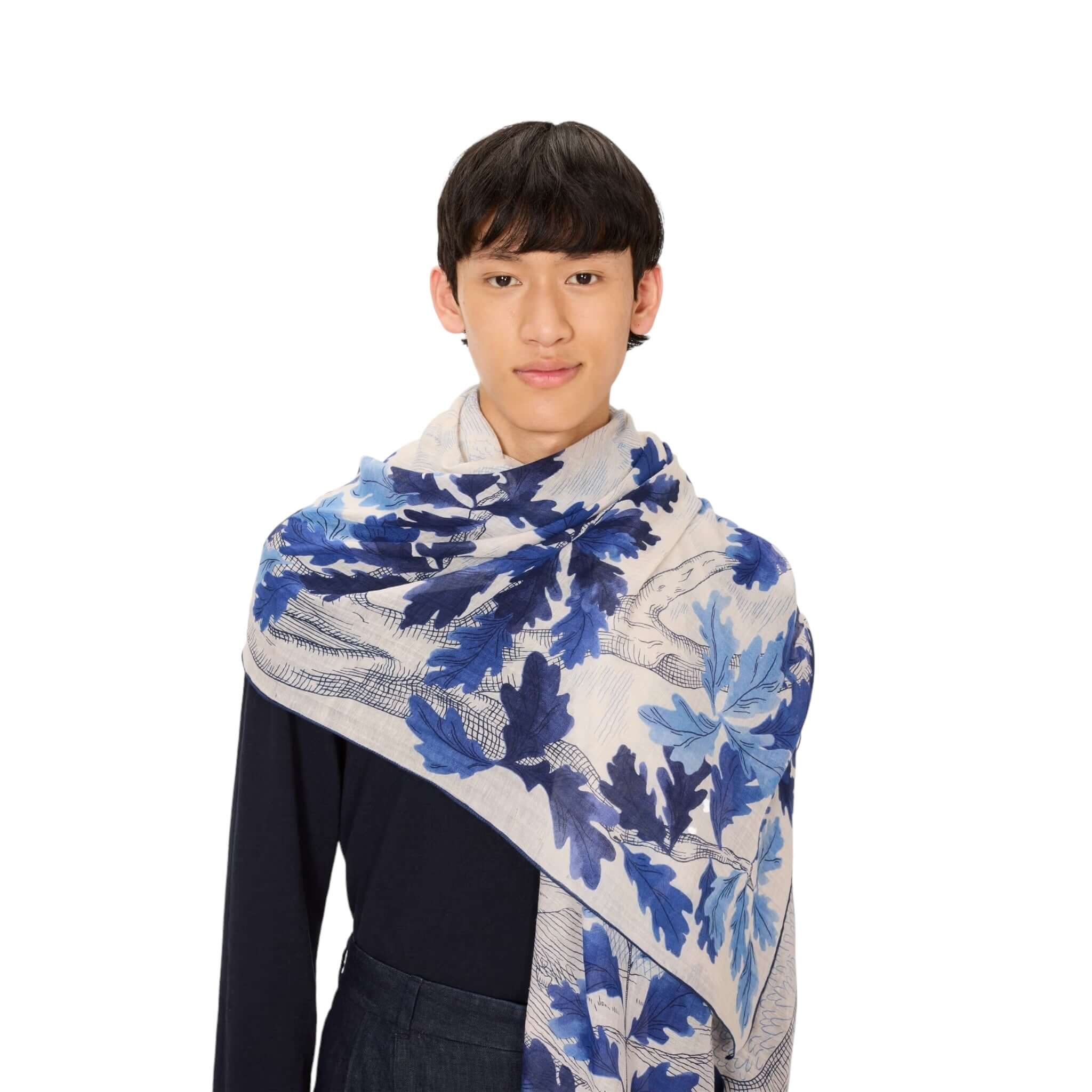 Young man wearing the hand-printed Sciarpa Amboise scarf with blue leaf design, showcasing its elegance and color finesse.